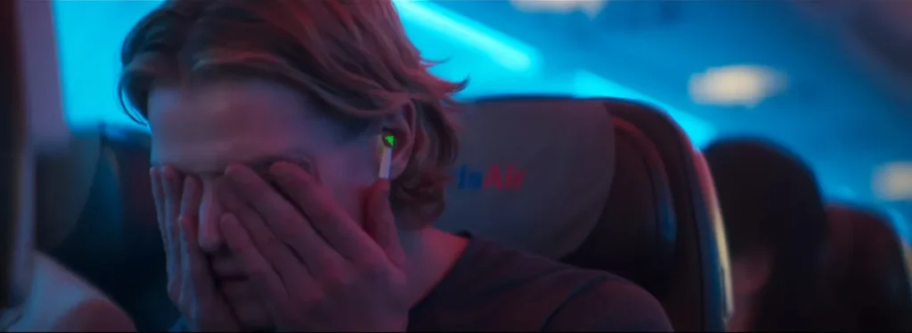 A man covering his face with his hands on a plane, from the official Clayface trailer