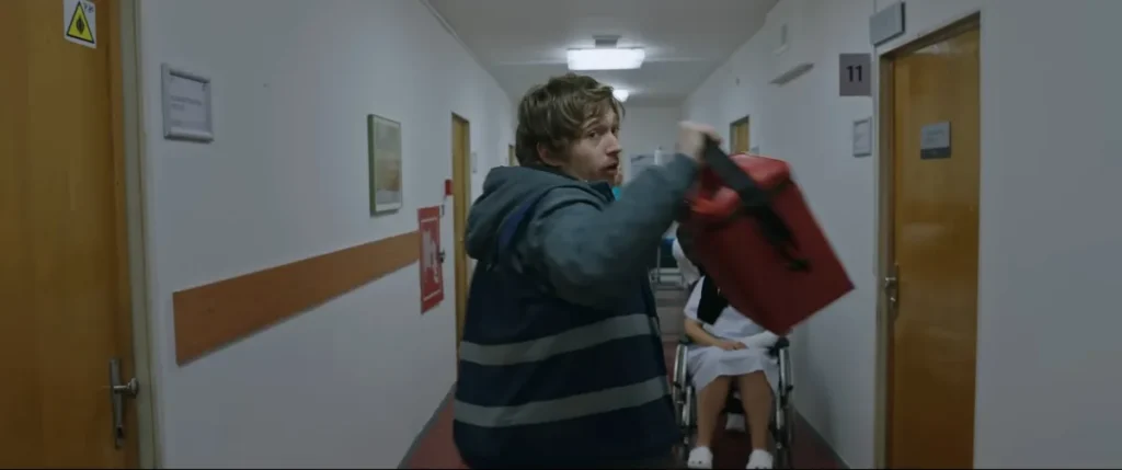 A medical courier carrying a red cooler down a hospital corridor, from the official Resident Evil trailer